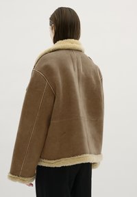 Giacca in suede marrone con colletti e polsini in shearling. Design oversize con cuciture visibili e una finitura morbida e testurizzata.