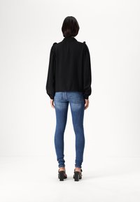Fekete puffujjú blúz lekerekített gallérral, párosítva kék skinny farmernadrággal és fekete blokk sarkú szandálokkal. Simább szövettextúra.