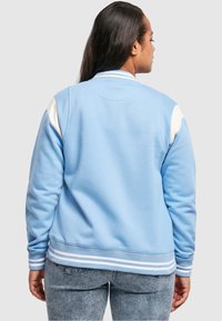 Gaiši zils džemperis ar baltām detaļām, ribotām aprocēm un apakšmalu. Gluda tekstūra, apaļas plecas un brīvs piegriezums.