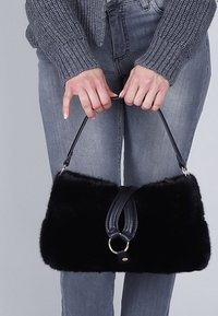 Borsa a tracolla nera in pelliccia sintetica con forma rettangolare, dotata di una maniglia in pelle e un'accattivante struttura ad anello in argento. Texture morbida e design strutturato.