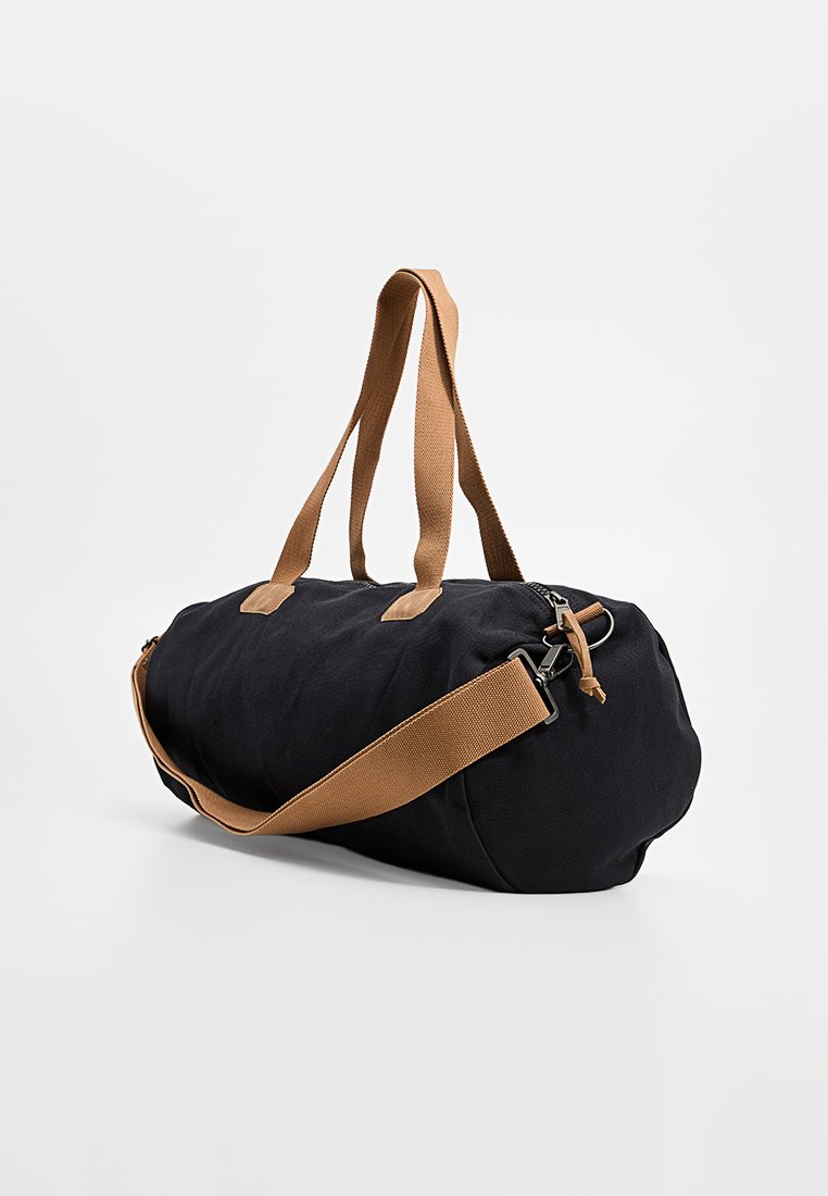 Zwarte cilindervormige sporttas met een bruine schouderriem en handvatten, met rits sluiting, rustend op een witte achtergrond.