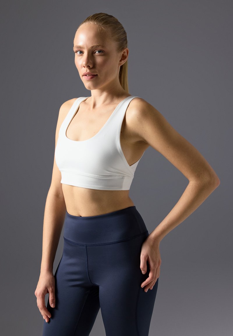 Hvit sports-bh med rund hals og brede stropper, kombinert med høytlivs marineblå leggins; glatt tekstur og atletisk design.