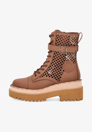 Botte marron à lacets avec panneaux latéraux en treillis, une sangle à boucle près de la cheville et une semelle épaisse et texturée.
