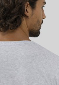 T-shirt grigio a maniche corte con collo a giro, texture morbida e leggero motivo melange. Focus sulla vista posteriore e sui dettagli del collo.