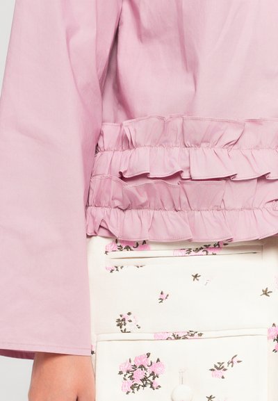 Różowa bluzka z falbaniastym dołem i warstwowym materiałem. W zestawieniu z kremowym elementem odzieży ozdobionym małymi różowymi kwiatowymi wzorami i kieszeniami.