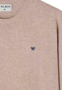 Suéter de punto beige hecho de una tela suave, con cuello redondo y un pequeño logo de tijeras azul oscuro en el lado izquierdo del pecho.