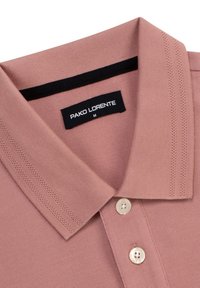 Koszulka polo w delikatnym różowym materiale o teksturowanym wykończeniu, z kołnierzykiem, trzema guzikami oraz czarną metką na szyi z napisem "PAKO LORENTE M."