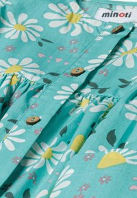 Türkises Kleid mit Blumenmuster, das weiße Gänseblümchen und gelbe Akzente zeigt. Holzknöpfe und geraffte Stoffdetails sorgen für Textur.