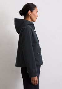 Ciemna, kapturowa kurtka o strukturalnym designie, z guzikami z przodu, kieszenią na piersi i gładką, matową teksturą.