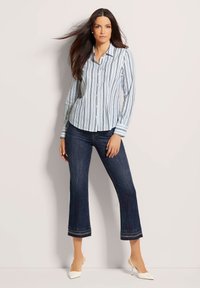 Gestreiftes Hemd in Hellblau, mit langen Ärmeln und abgerundetem Saum. Kombiniert mit dunkelblauen, cropped Jeans, die an den Rändern ausgefranst sind.