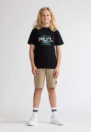 T-shirt noir à motifs verts, short cargo beige, baskets blanches et chaussettes rayées. L'enfant se tient debout, les mains le long du corps.
