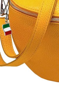 Geel leren tas met gestructureerd oppervlak, voorzien van een zilveren rits en een sleutelhanger met een kleine Italiaanse vlag in rood, wit en groen.
