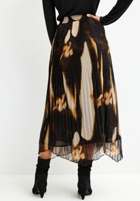 Plisseret midi-nederdel i letvægts chiffon med en blanding af abstrakte mønstre i sort, brunt og beige; har høj talje og lagdelt tekstur.