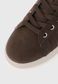 Καφέ αθλητικό παπούτσι με απαλό επάνω μέρος από σουέντ, σχέδιο με κορδόνια και υφασμένα κορδόνια, και λαστιχένια σόλα με λευκή περίμετρο.