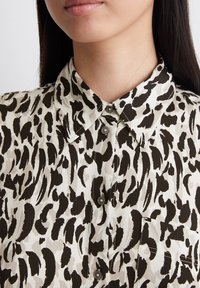 Kurzärmliges Hemd mit Kragen aus leichtem Stoff. Verfügt über einen hochkontrastierenden schwarz-weißen Tierdruck, eine einzelne Brusttasche und eine Knopfleiste.