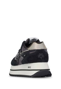 Sneaker in suede nero e grigio con superficie testurizzata, accenti metallici riflettenti e suola bianca spessa con una striscia nera.