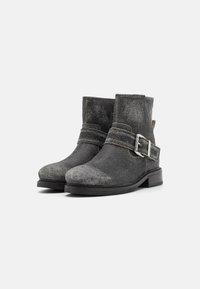 Botines de cuero negro con un acabado desgastado, que cuentan con una correa lateral con una hebilla de plata y un diseño de punta redondeada.