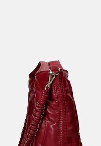 Borsa a mano in pelle rossa con una finitura testurizzata, dotata di una tracolla intrecciata e hardware in argento. Il design include dettagli cuciti.