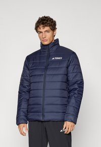 Chaqueta tipo plumas en color navy con un alto cuello, patrón de acolchado horizontal, cremallera frontal y logo de Terrex en el lado izquierdo del pecho.