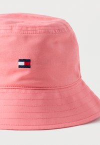 Ροζ βαμβακερό καπέλο τύπου bucket με φαρδύ γείσο. Περιλαμβάνει ραμμένες λεπτομέρειες και ένα μικρό κεντημένο λογότυπο σε ναυτικό μπλε, κόκκινο και λευκό.