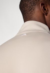 Beeži polo särk sileda tekstuuriga, millel on volditud krae ja väike valge logo selja peal.