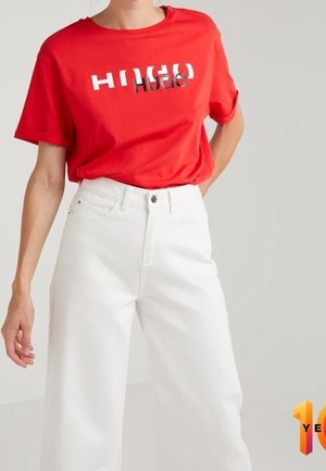Červené tričko s krátkým rukávem a kontrastním černo-bílým logem "HUGO"; kombinováno s bílými širokými džíny s vysokým pasem.