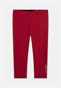 Red leggings made of stretchy fabric with a fitted design. Features a black and red leopard-print waistband; "GUESS" logo in gold accent.