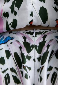Tissu à motif floral avec des feuilles vertes, des accents roses et des détails bleus. Comprend une fermeture éclair blanche visible à la taille.