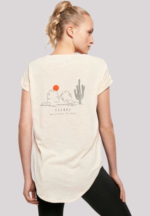Light beige short-sleeve t-shirt featuring a graphic design of a sunset, mountains, and a cactus on the back. Curved hem along the bottom.
