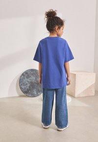 Modra bombažna majica s kratkimi rokavi, okroglim izrezom in sproščenim krojem, kombinirana z širokimi kavbojkami in belimi čevlji.