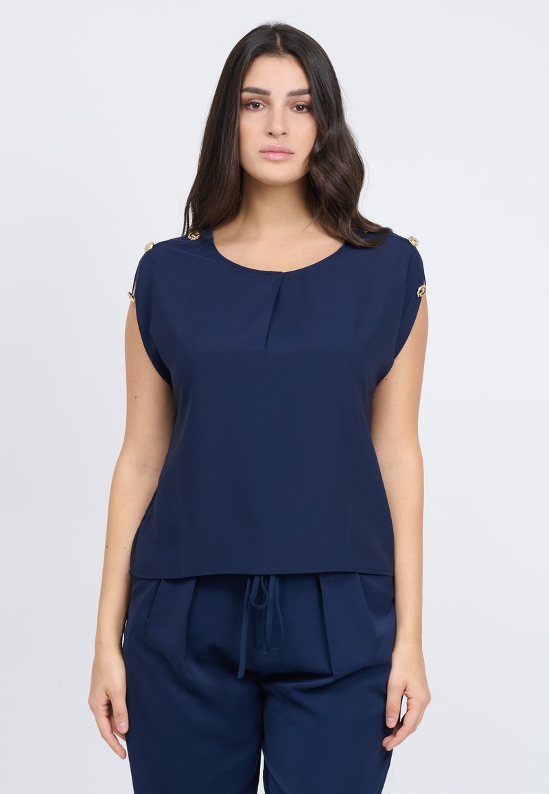 Blusa blu navy con scollo tondo, maniche corte e dettagli con bottoni dorati sulle spalle. Realizzata in tessuto morbido con una vestibilità rilassata.