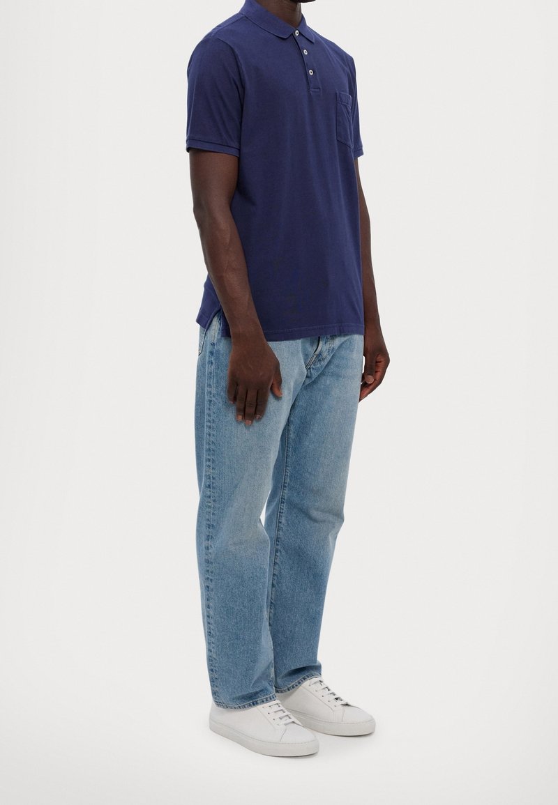 Námořnická polokošile s krátkými rukávy a kapsou, spárovaná s světle modrými džíny a bílými teniskami. Polokošile má na límci knoflíkovou ozdobu.