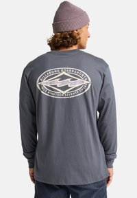 Langärmliges graues Shirt aus Baumwolle mit einem Rückenlogo-Design, das Wellen in einem Oval zeigt. Weicher Stoff und lockere Passform.