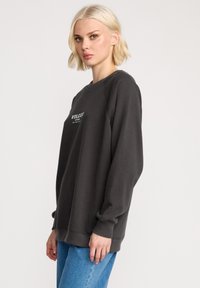 Donkergrijze sweatshirt met een ronde halslijn, geribbelde manchetten en zoom. Bevat het "VOLCOM"-logo in het wit op de voorkant. Zachte stoftextuur.