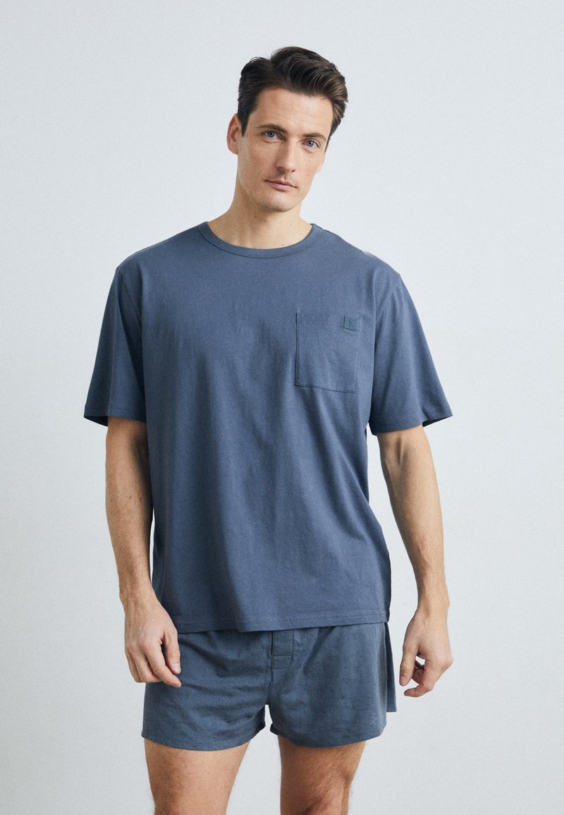 Marineblaue katoenen T-shirt met korte mouwen en een borstzak, gecombineerd met bijpassende korte broek. Eenvoudig ontwerp, zachte textuur, comfortabele pasvorm.