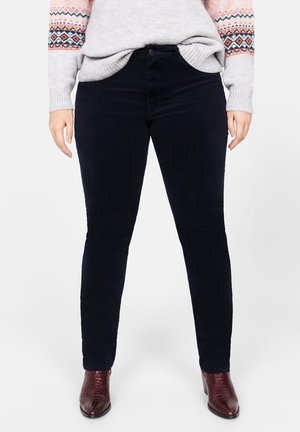 Schmal geschnittene schwarze Hose, kombiniert mit einem hellgrauen gemusterten Pullover und dunkelroten, strukturierten Stiefeletten.
