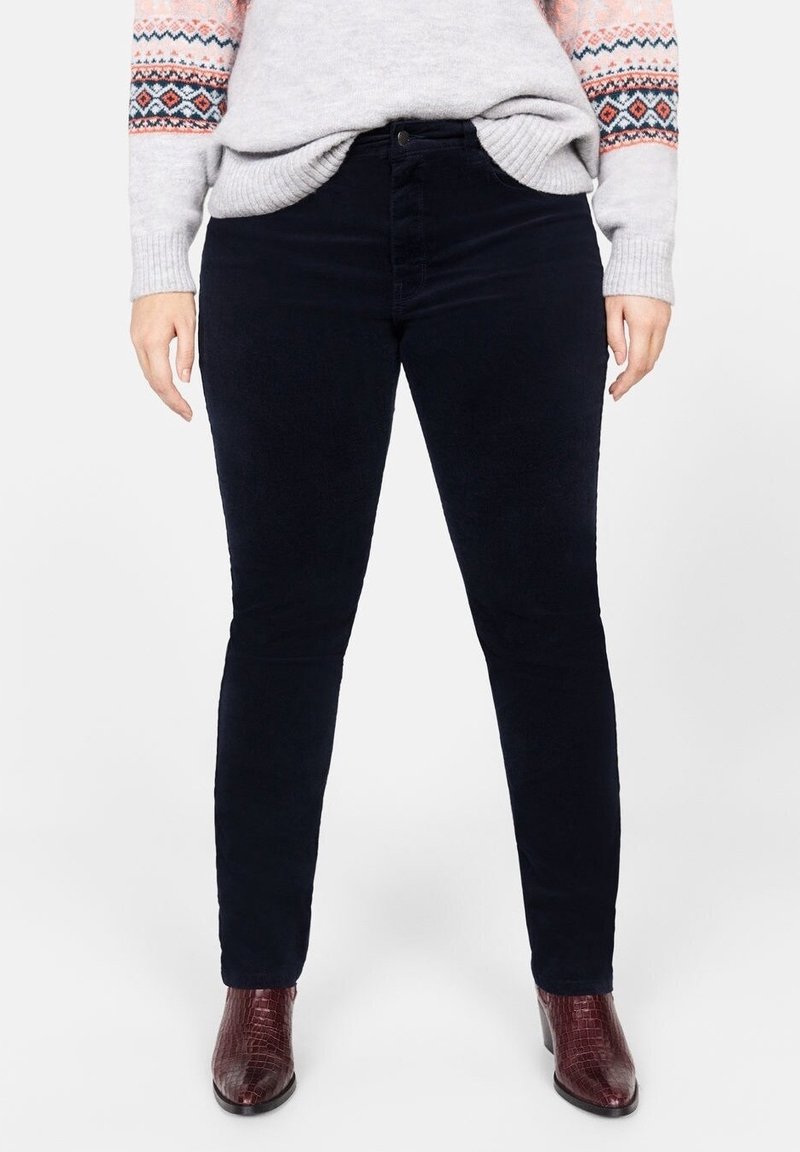 Pantalon noir slim porté avec un pull gris clair à motifs et des bottines texturées rouge foncé.