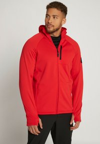 Giacca rossa con zip e cappuccio, dotata di tasca sul petto con zip, texture morbida e design aderente. Accenti in hardware nero a contrasto.