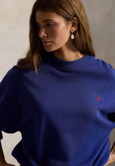 Μπλε υπερμεγέθη φούτερ με υφή και ριμπ σε γιακά, με μικρό κόκκινο λογότυπο στο αριστερό στήθος.