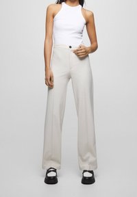 Haut à col licou blanc associé à un pantalon large couleur crème avec fermeture à boutons, texture lisse et léger éclat. Sandales à plateforme noires.