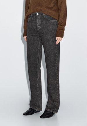 Jean en denim noir avec une finition légèrement délavée, coupe droite, conception à cinq poches et fermeture à bouton, associé à un pull marron.