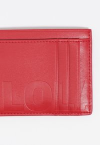 Cartera de cuero rojo con una textura suave, que presenta letras en relieve y múltiples ranuras para tarjetas, mostrando un diseño rectangular y elegante.