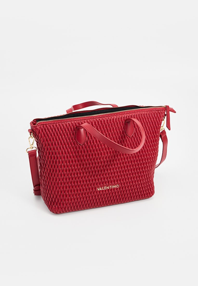 Sac à main texturé rouge avec fermeture éclair sur le dessus, deux poignées et une bandoulière amovible. Détail du logo doré sur le devant.