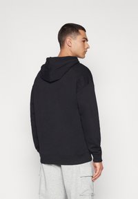 Sort hættebluse i blødt stof med en afslappet pasform og ribbede manchetter, parret med grå cargo bukser for et afslappet look.