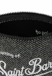 Ingrandimento di una borsa in tessuto a spina di pesce nera e grigia con una cerniera nera e testo bianco in corsivo parzialmente visibile.