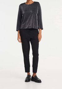 Top negro brillante de manga larga con cuello redondo, combinado con pantalones negros ajustados con cremalleras en los puños y mocasines negros.