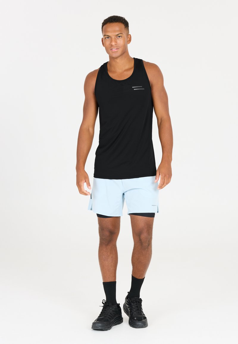 Svart linne, ljusblå shorts med sidoklipp, svarta strumpor och svarta sneakers. Linnet har subtila vita linjeaccenter.