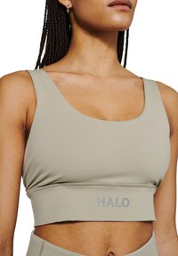 Jasnozielony stanik sportowy wykonany z gładkiego materiału, z szerokim pasem i napisem "HALO" w szarym kolorze blisko dolnej krawędzi. Posiada plecy w stylu racerback.