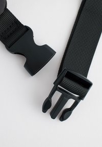 Boucle à libération latérale en plastique noir avec des sangles en nylon noir texturé sur un fond clair.