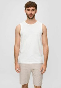 Weißes ärmelloses Tanktop aus weichem Stoff, kombiniert mit hellbraunen Shorts. Einfaches Design mit einem runden Halsausschnitt und minimalen Nähdetails.